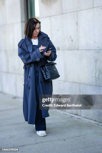 Guest wears a white t-shirt, a gray dark oversized long coat, a black shiny leather crossbody bag from Saint Laurent, black pants, white leather...