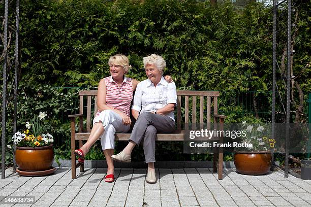 two older women sit on a bench in a garden - adult woman garden flower stock-fotos und bilder