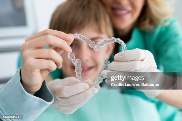 boy and dentist holding an invisible heart shaped brace - odontología cosmética fotografías e imágenes de stock