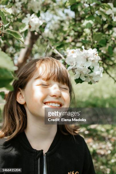 portrait of a happy teenage girl in spring next to a flowering tree enjoying the bright sun, putting her face under the rays - face happy sun stockfoto's en -beelden