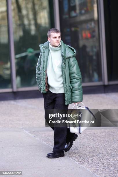 Guest wears a mint green wool turtleneck pullover from Ami, a dark green shiny leather hoodie puffer jacket, black large suit pants, a white and...