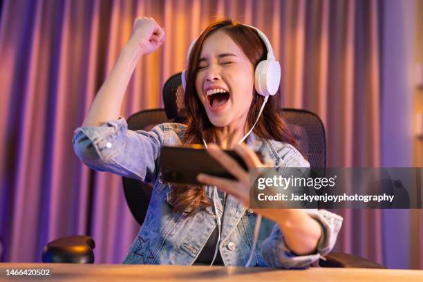 excited young asian woman playing game at her home - jeu mobile photos et images de collection