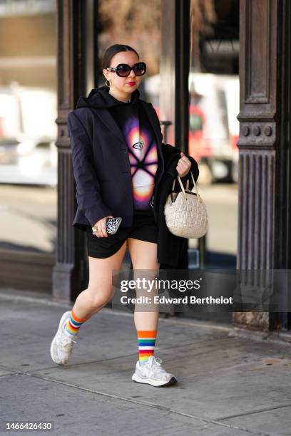 Guest wears black sunglasses from Ganni, gold earrings, a black with purple and pink print pattern hoodie sweater, a black blazer jacket, a beige...