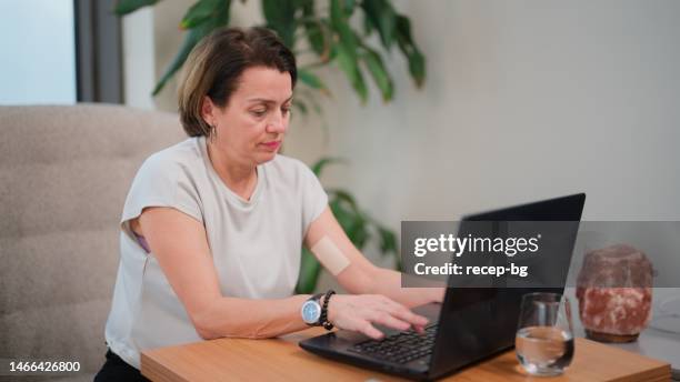 woman using laptop with hormone replacement therapy applied on her arm - transdermal stock pictures, royalty-free photos & images