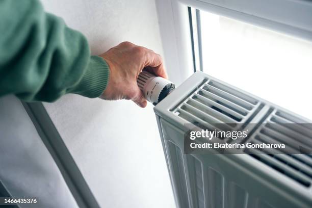 close-up of female hands regulating the thermostat on the radiator. - cold indoors stockfoto's en -beelden