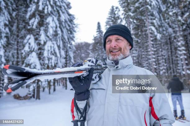 fröhlicher mann im skioutfit und skiern auf der schulter auf der skipiste. - männer über 30 stock-fotos und bilder