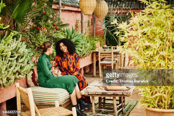 wide shot of smiling sisters relaxing in hotel rooftop garden - arab family in hotel stock-fotos und bilder