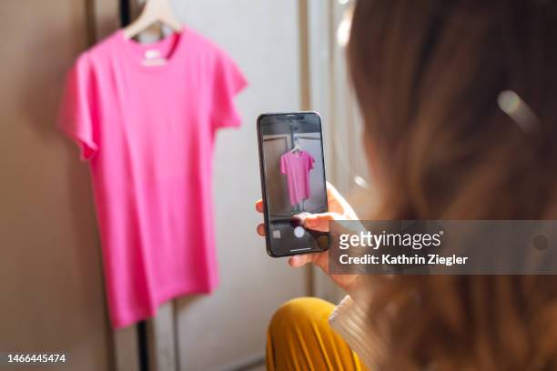 woman taking a picture of a pink t-shirt for secondhand sale - second hand stock-fotos und bilder