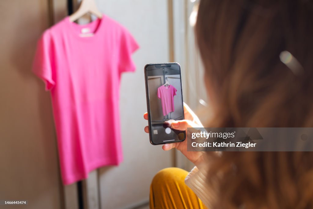 Woman taking a picture of a pink t-shirt for secondhand sale