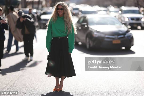 Emili Sindlev seen wearing a black pleated midi skirt, a green oversized sweater and orange Prada heels before the Coach show on February 13, 2023 in...