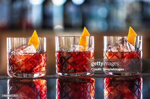 three modern glasses of negroni cocktail and gin short drink with sweet vermouth, red bitter liqueur and dried orange peel on bar counter. - rum tasting stock pictures, royalty-free photos & images
