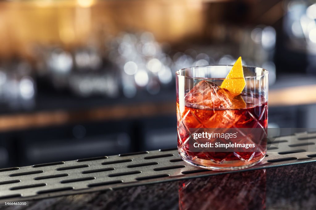 Negroni classic cocktail and gin short drink with sweet vermouth, red bitter liqueur and dried orange peel on bar counter.