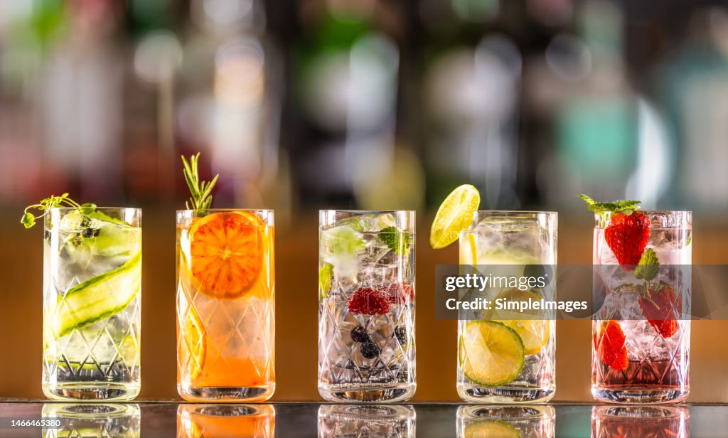 Five gin tonic cocktails in wine glasses on bar counter in pup or restaurant.