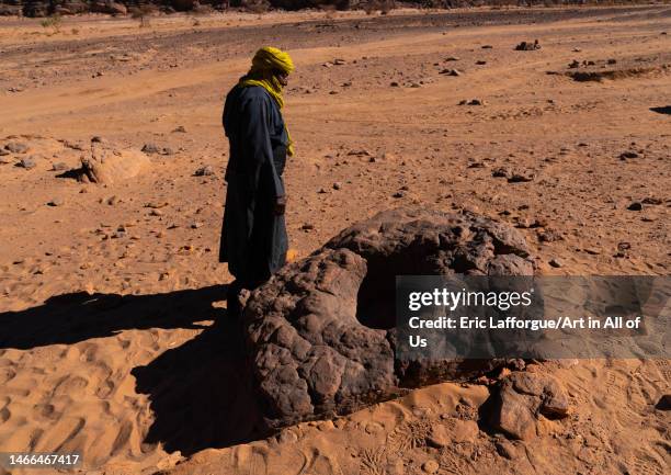 Tuareg man in front of a rock to store water in the desert, Tassili N'Ajjer National Park, Tadrart Rouge, Algeria on December 30, 2022 in Tadrart...