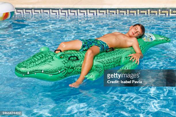 boy resting on inflatable crocodile at pool - pool boat stockfoto's en -beelden