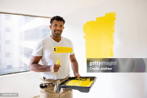 house painter painting a wall yellow using a paint roller - huisschilder stockfoto's en -beelden