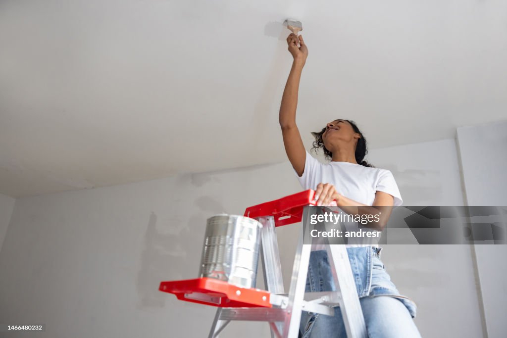 Happy woman painting the ceiling of her house using a ladder