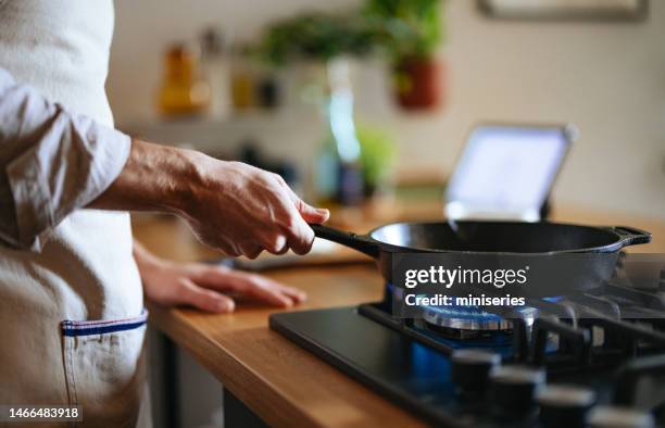 foto ravvicinata delle mani dell'uomo che preparano il pranzo in una padella a casa - fornello foto e immagini stock