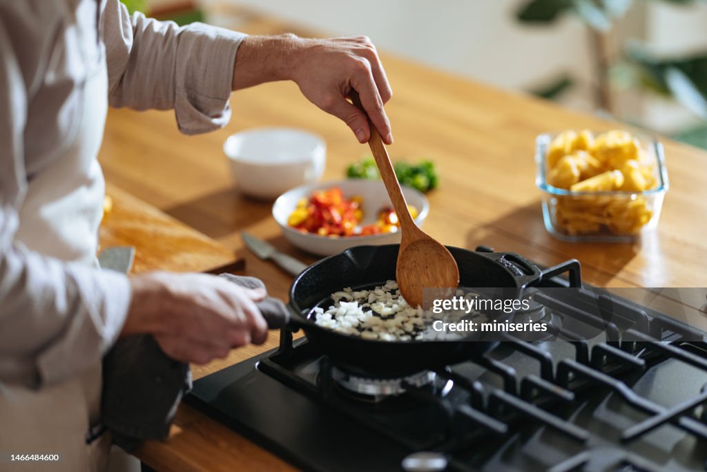 Foto de cerca de las manos de Manâs preparando el almuerzo en la sartén en casa