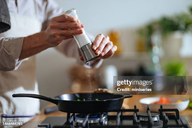 close up foto das mãos do homem colocando sal na frigideira em casa - sal de cozinha - fotografias e filmes do acervo