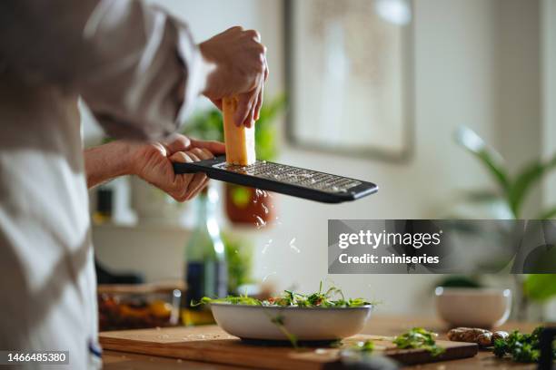 nahaufnahme foto von männerhänden, die käse in einem salat zu hause reiben - reiben stock-fotos und bilder