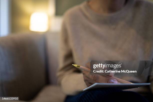 black woman holding note pad & pencil sitting on sofa - dear diary stock pictures, royalty-free photos & images