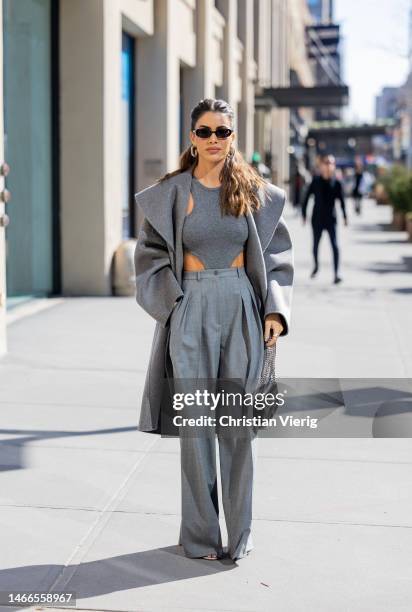 Camila Coelho wears grey pants, coat, body, sunglasses, black bag outside Michael Kors New York Fashion Week during on February 15, 2023 in New York...