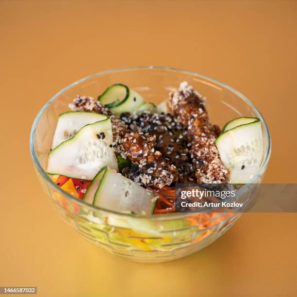 chicken with teriyaki sauce and garnish of carrots, peppers and cucumbers. asian dish. eastern cuisine. dish in transparent bowl. orange background. side view - teriyaki foto e immagini stock