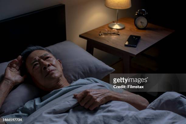 depressed senior asian man lying in bed cannot sleep from insomnia - insomnia stockfoto's en -beelden