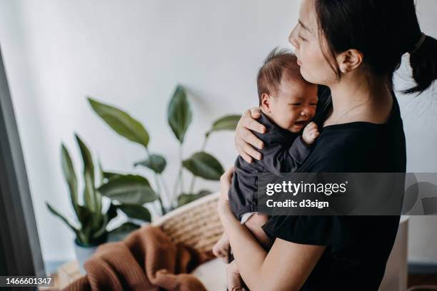 a loving young asian mother carrying her newborn baby girl in arms, consoling and comforting her crying baby. hunger and discomfort. love and care. motherhood and parenthood concept - baby depression fotografías e imágenes de stock