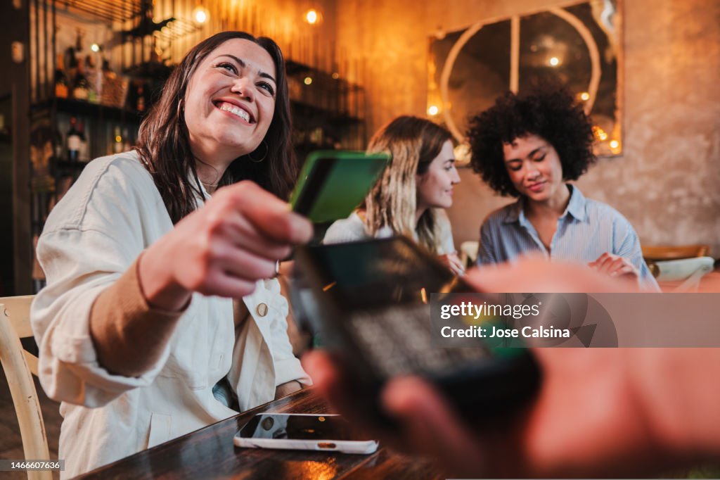 Happy young woman paying bill with a contactless credit card in a restaurant. Female smiling holding a creditcard and giving a payment transaction to the cashier.