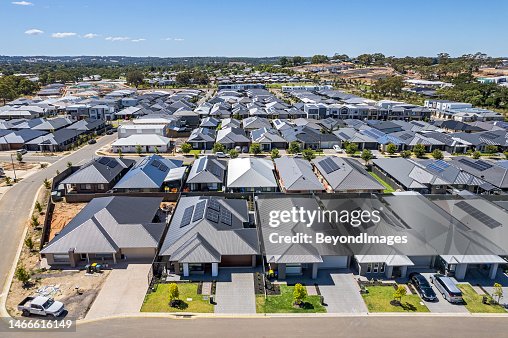 Low aerial close view new dense rural housing development, mostly grey roofing, some green landscaping, young trees Low aerial close view new dense rural housing development, mostly grey roofing, some green landscaping, young trees
