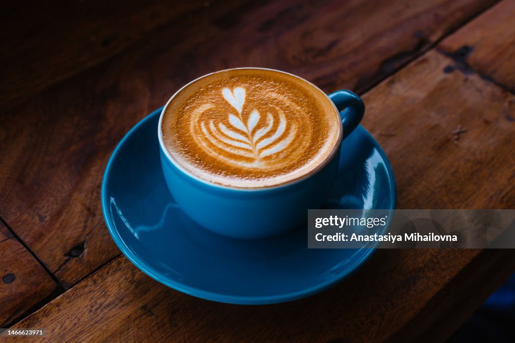 Cappuccino in a blue ceramic mug on a wooden table side view