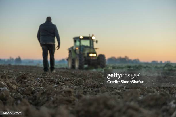 male farmer with short brown hair,walking in the direction to his tractor,standing next to his agricultural field in the evening with lights turned on, - farm stock pictures, royalty-free photos & images