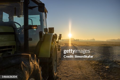 Tractor parked on an agricultural path in the evening during sunset with back lit and sun at the horizon