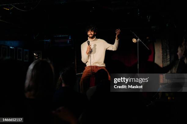 smiling young male comedian performing stand-up on stage in theater - comedian foto e immagini stock