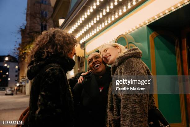 happy multiracial female friends greeting outside movie theater at night - arab people laugh stockfoto's en -beelden