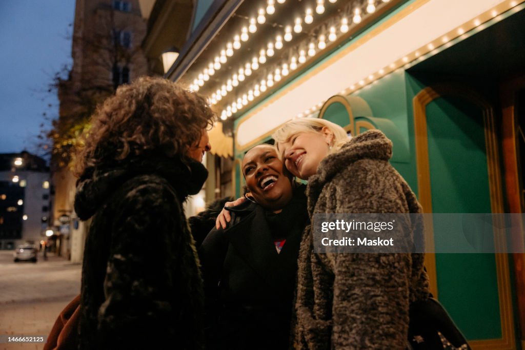 Happy multiracial female friends greeting outside movie theater at night