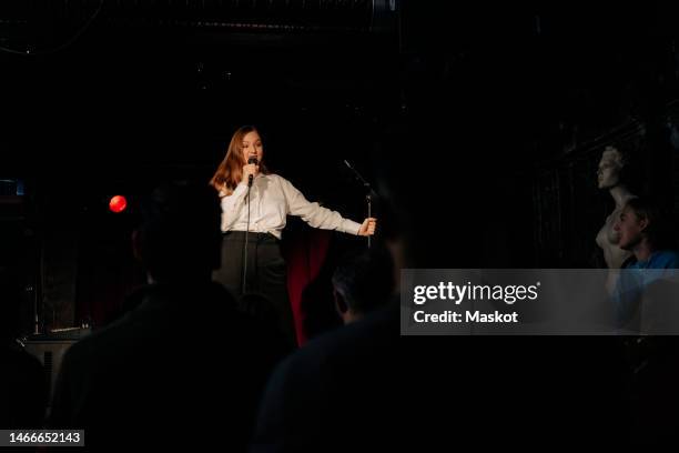 young female comedian performing stand-up with microphone on stage at theater - stand up comedian - fotografias e filmes do acervo