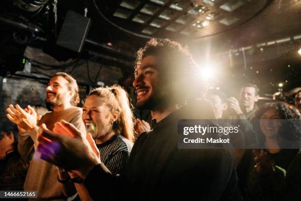 cheerful multiracial male and female audience giving standing ovation at illuminated theater - aplaudindo - fotografias e filmes do acervo