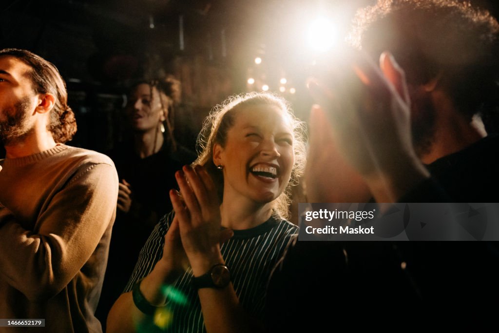 Cheerful woman giving standing ovation by male friends at illuminated theater