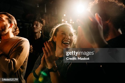 Cheerful woman giving standing ovation by male friends at illuminated theater Cheerful woman giving standing ovation by male friends at illuminated theater