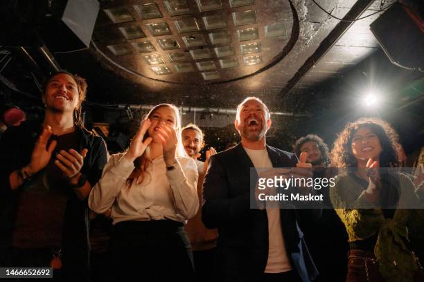 cheerful multiracial male and female audience giving standing ovation at theater - ovación de pie fotografías e imágenes de stock