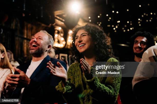happy audience laughing and clapping while watching comedy stage show in illuminated theater - representación teatral fotografías e imágenes de stock