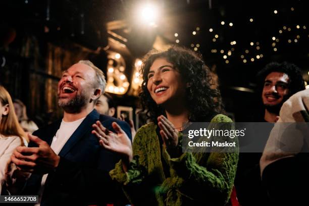 happy audience laughing and clapping while watching comedy stage show in illuminated theater - actuacion fotografías e imágenes de stock