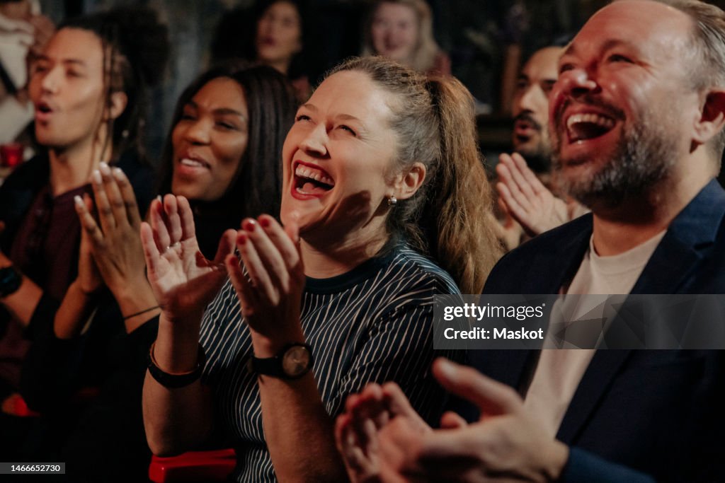 Multiracial audience laughing and applauding while watching comedy stage show in theater