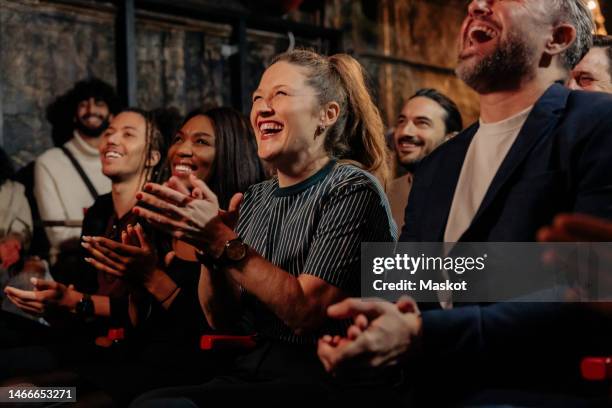 cheerful multiracial friends laughing while watching comedy stage show in theater - applauding fotografías e imágenes de stock