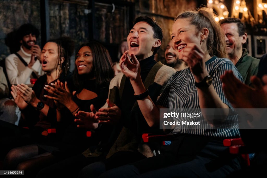 Happy multiracial friends laughing while enjoying comedy show at stage theater