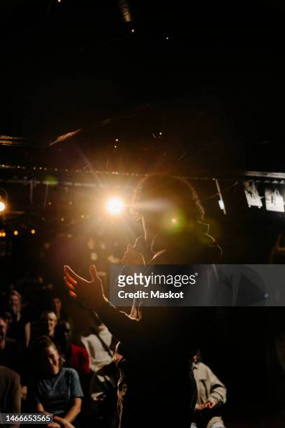 young man performing stand-up comedy for audience at illuminated stage theater - comedian audience stock pictures, royalty-free photos & images