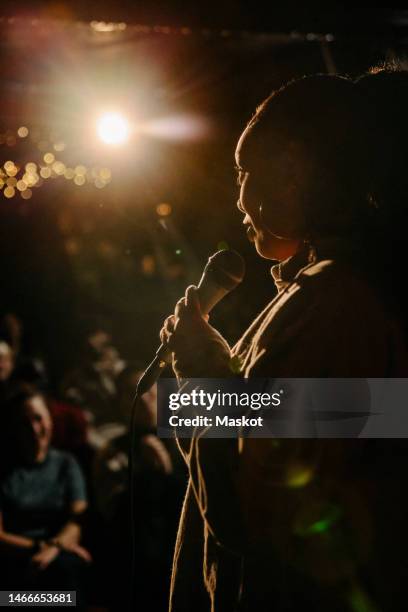 woman performing stand-up comedy at illuminated amateur theater - stand up comedy stock-fotos und bilder
